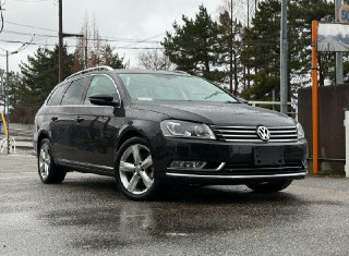 Чёрный Volkswagen Passat Variant — вид спереди и сбоку на мокрой парковке, видно фирменную решётку радиатора и колесные диски автомобиля.