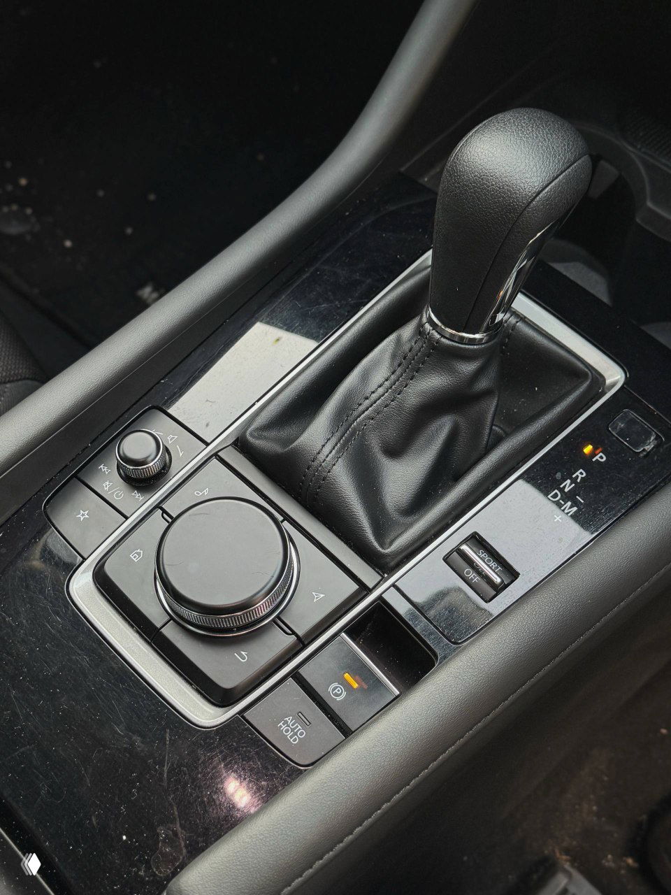 Селектор автоматической коробки передач Mazda 3 2020 и контроллер мультимедиа на центральной консоли; вид поверхности и органов управления.