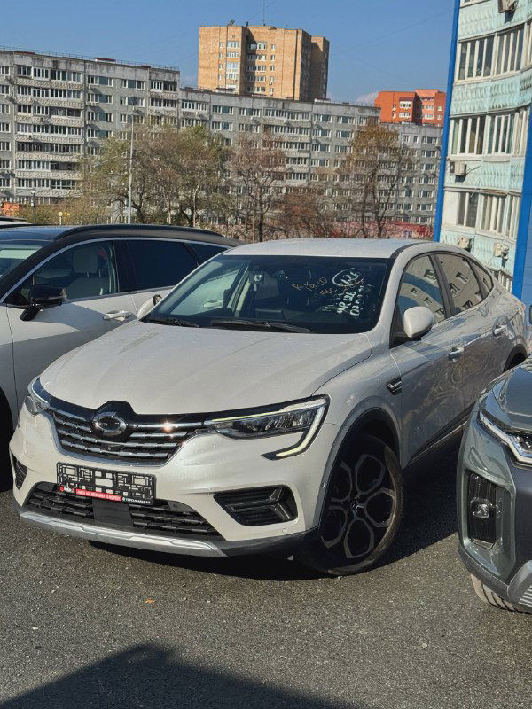 Белый Renault Samsung XM3 — внешний вид спереди три четверти на городской парковке между автомобилями; видны фары, решётка и легкосплавные диски.