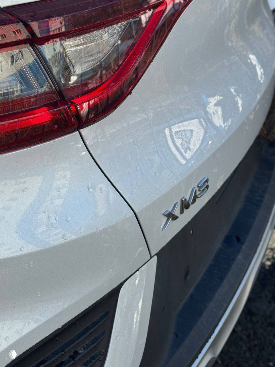 Крупный план задней части Renault Samsung XM3 с шильдиком модели «XM3», видны задний бампер, фонарь и краска автомобиля с каплями воды.