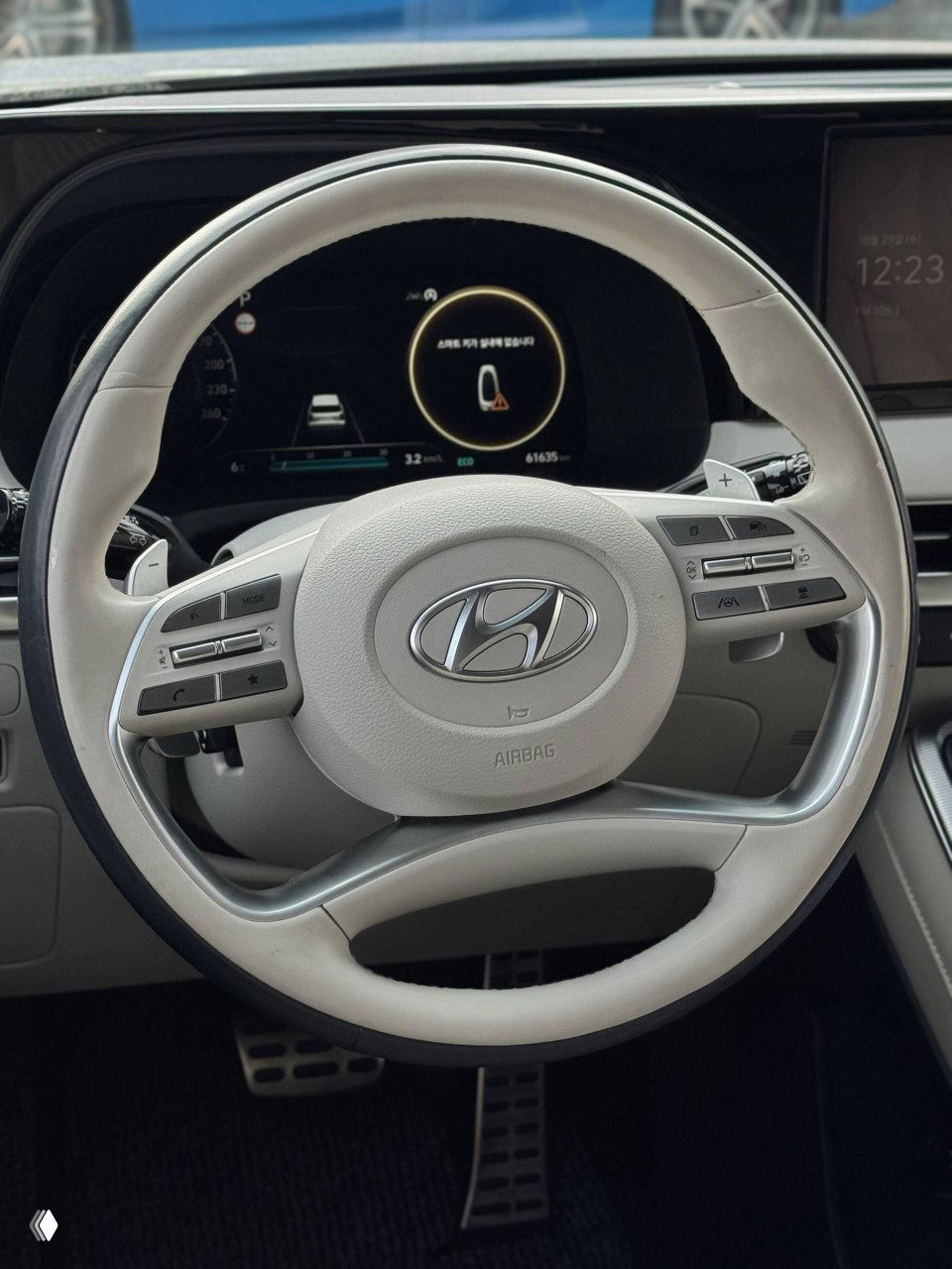 Крупный план белого кожаного рулевого колеса Hyundai Palisade с эмблемой, мультирулевыми кнопками и подрулевыми лепестками, интерьерная съёмка салона при осмотре.