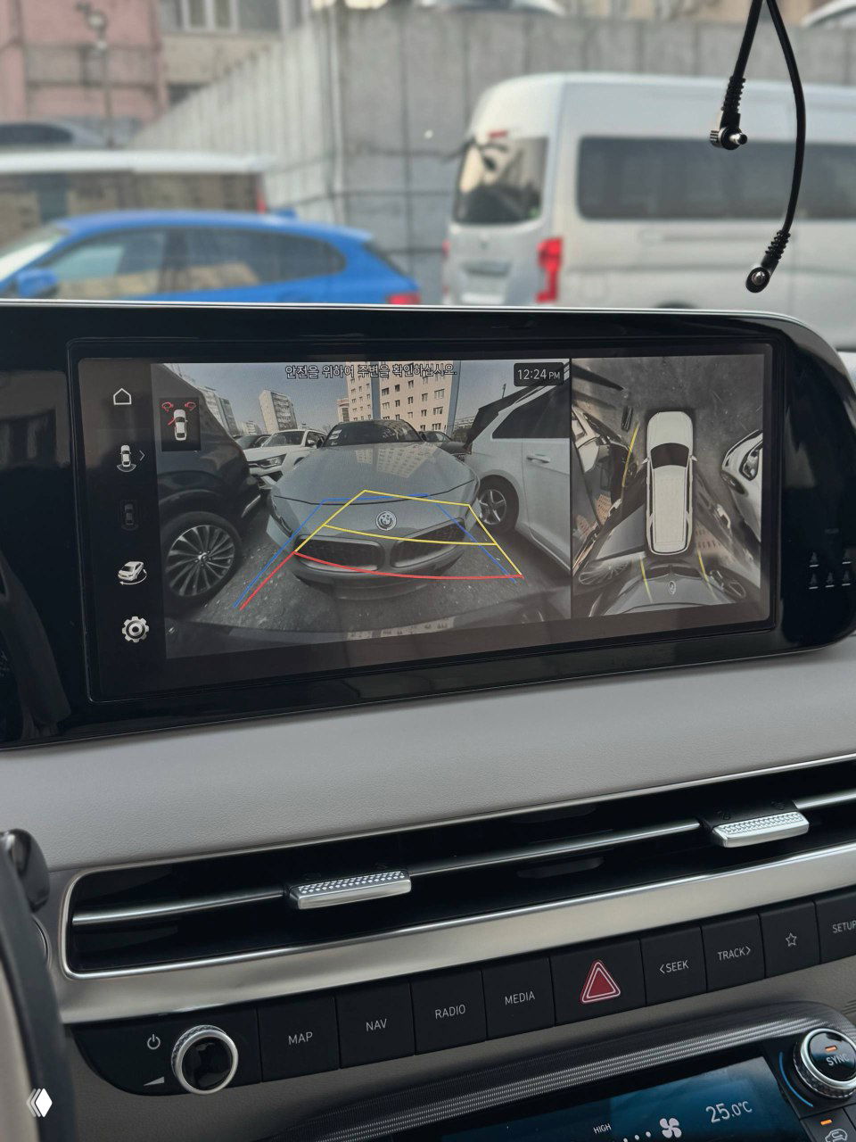 Экран мультимедиа показывает изображение с камеры заднего вида и круговой обзор автомобиля с парковочной разметкой — демонстрация системы помощи при парковке.