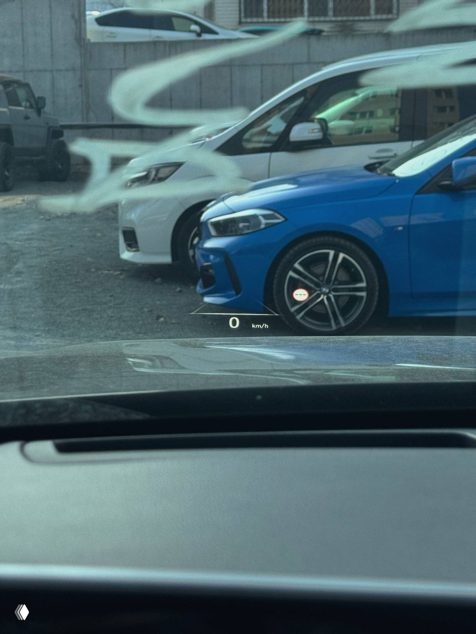 Вид через лобовое стекло с проекцией HUD на стекле, отображается скорость 0 km/h, кадр показывает парковку и соседние автомобили рядом с Palisade.