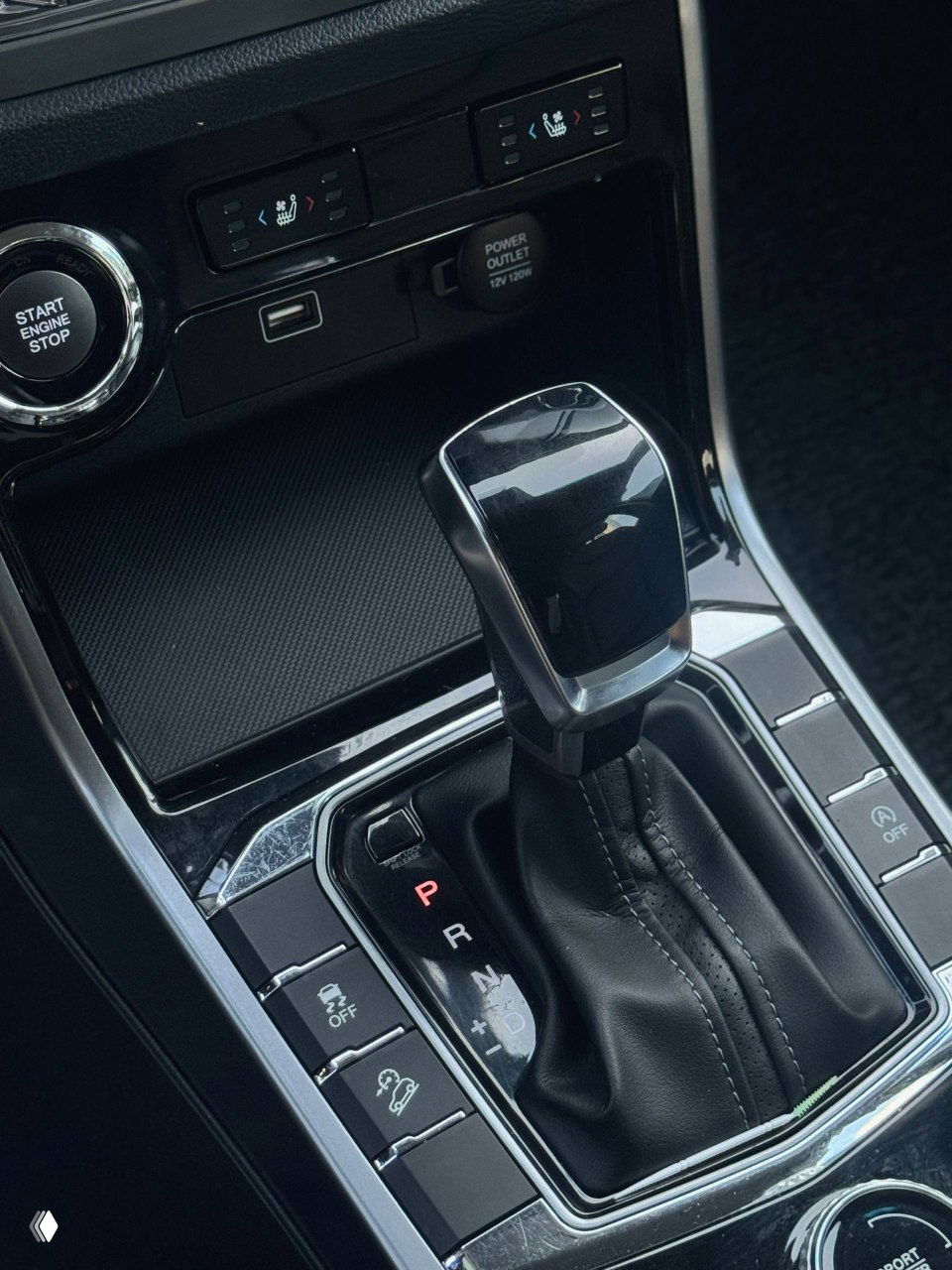 Крупный план селектора АКПП и блока дополнительных кнопок — чёрный глянцевый кожух селектора и посадочные места для гаджетов.