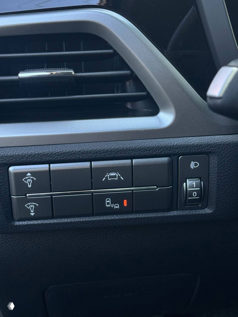 Панель управляющих кнопок у водителя: ассистенты полосы, подсветка и регулировка фар в зоне приборной доски, крупный план.
