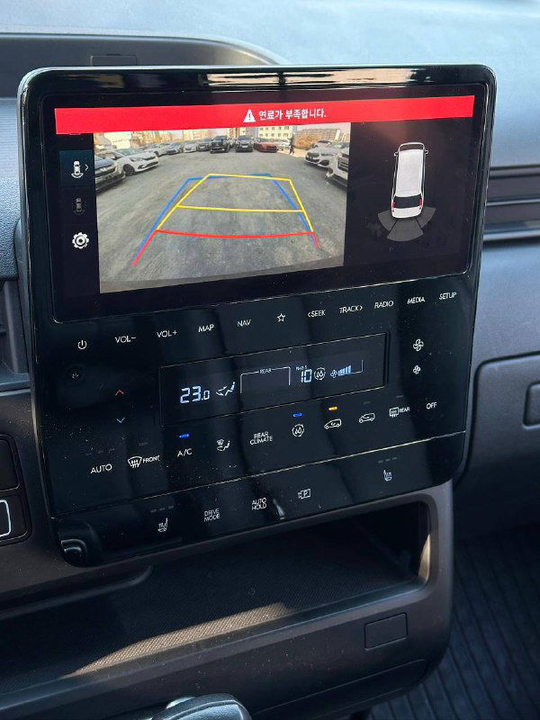 Мультимедийный экран Hyundai Staria показывает изображение камеры заднего вида; под экраном элементы климат-контроля и сенсорные кнопки панели.