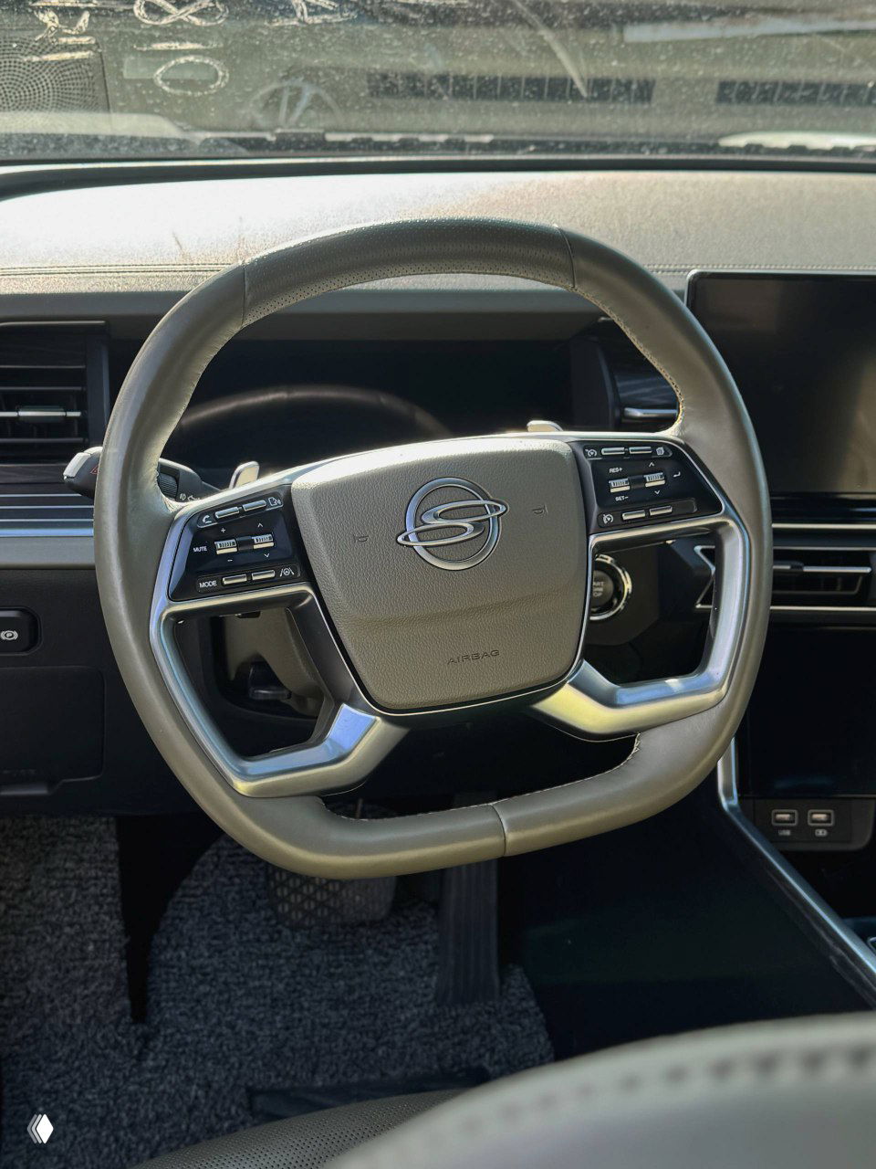 Руль SsangYong Torres крупным планом: множество кнопок управления, хромированные вставки, видимый логотип марки на подушке безопасности и текстура обивки.