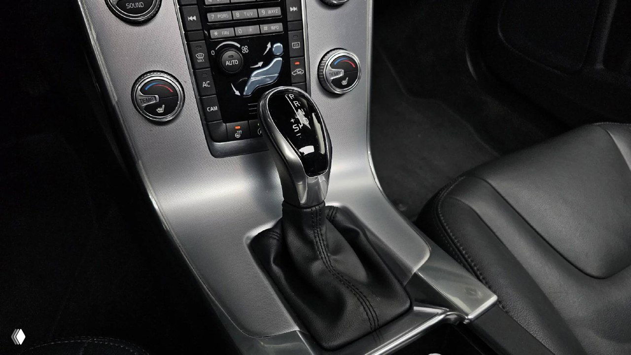 Крупный план рычага АКПП Aisin и части центральной консоли Volvo S60, видны элементы управления климатом и окантовка.