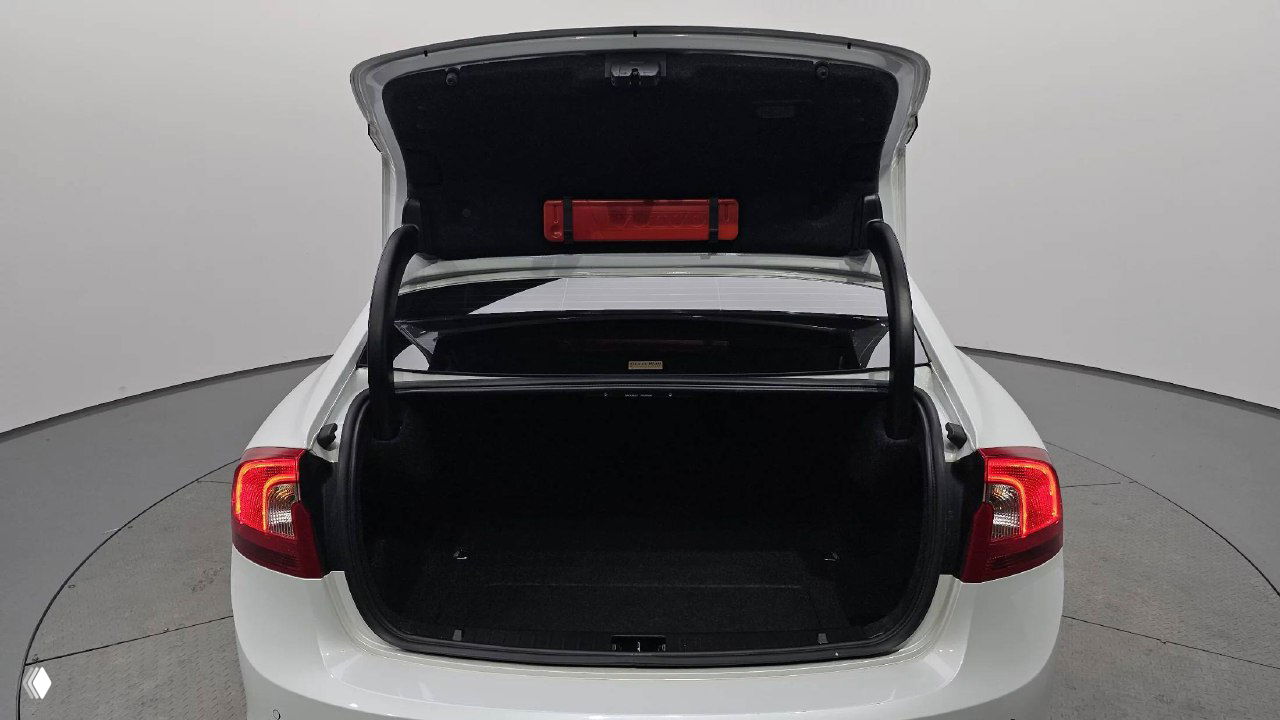 Открытый багажник белого Volvo S60 на подиуме дилера, видно внутреннее пространство грузового отсека и уплотнения крышки.