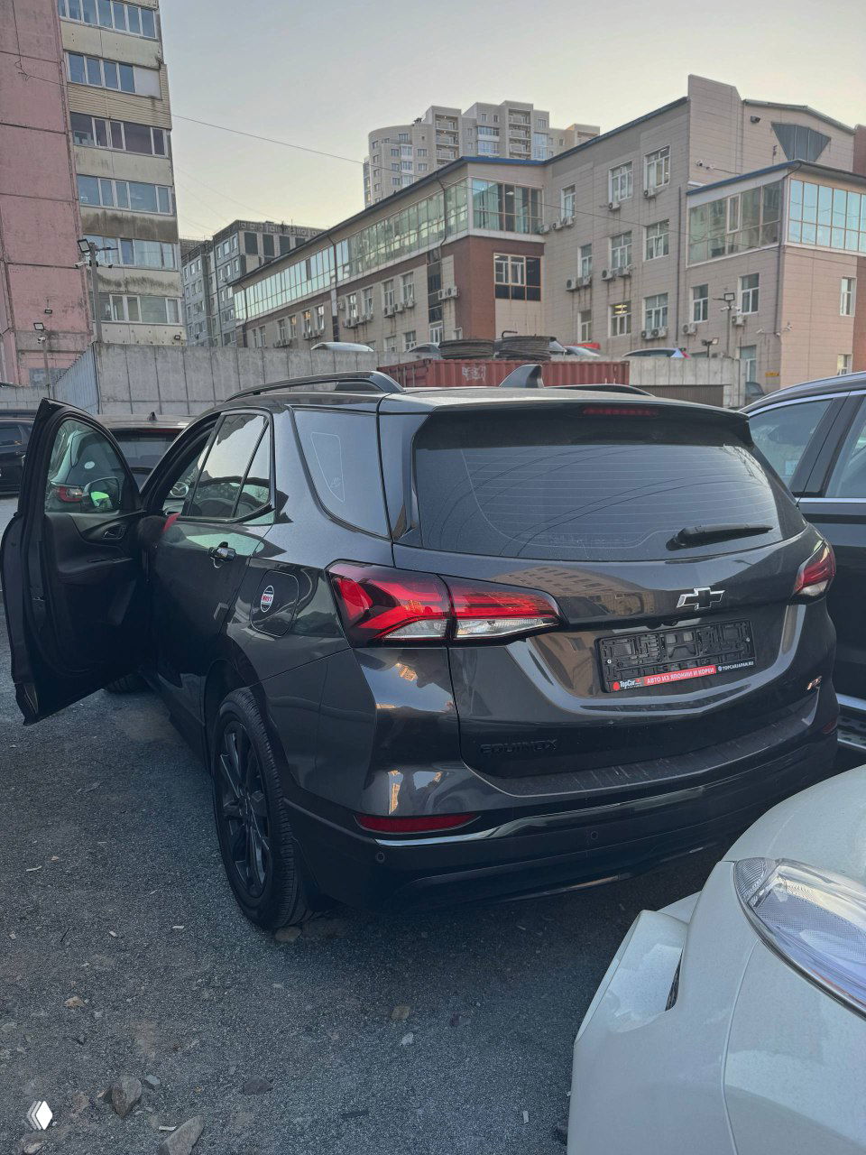 Задняя часть Chevrolet Equinox 2022 — вид сзади на паркинге, открыт левый задний дверной проём; чёрный/тёмный кузов и временные пометки на стёклах, общий контекст.