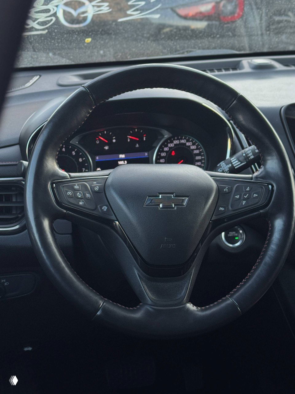 Рулевое колесо Chevrolet Equinox с фирменной эмблемой, вид на панель приборов и кнопки управления на спицах; чёрная отделка салона и показания приборов на дисплее.