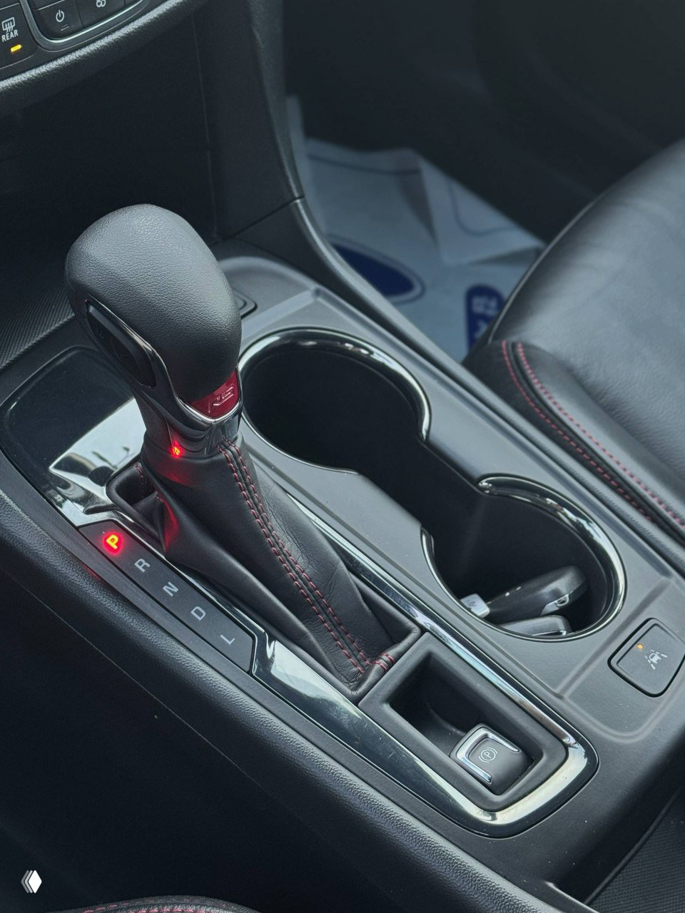 Рычаг автоматической коробки передач и центральная консоль Chevrolet Equinox, кожаная оплётка с красной прострочкой, подстаканники и площадка между сиденьями крупным планом.