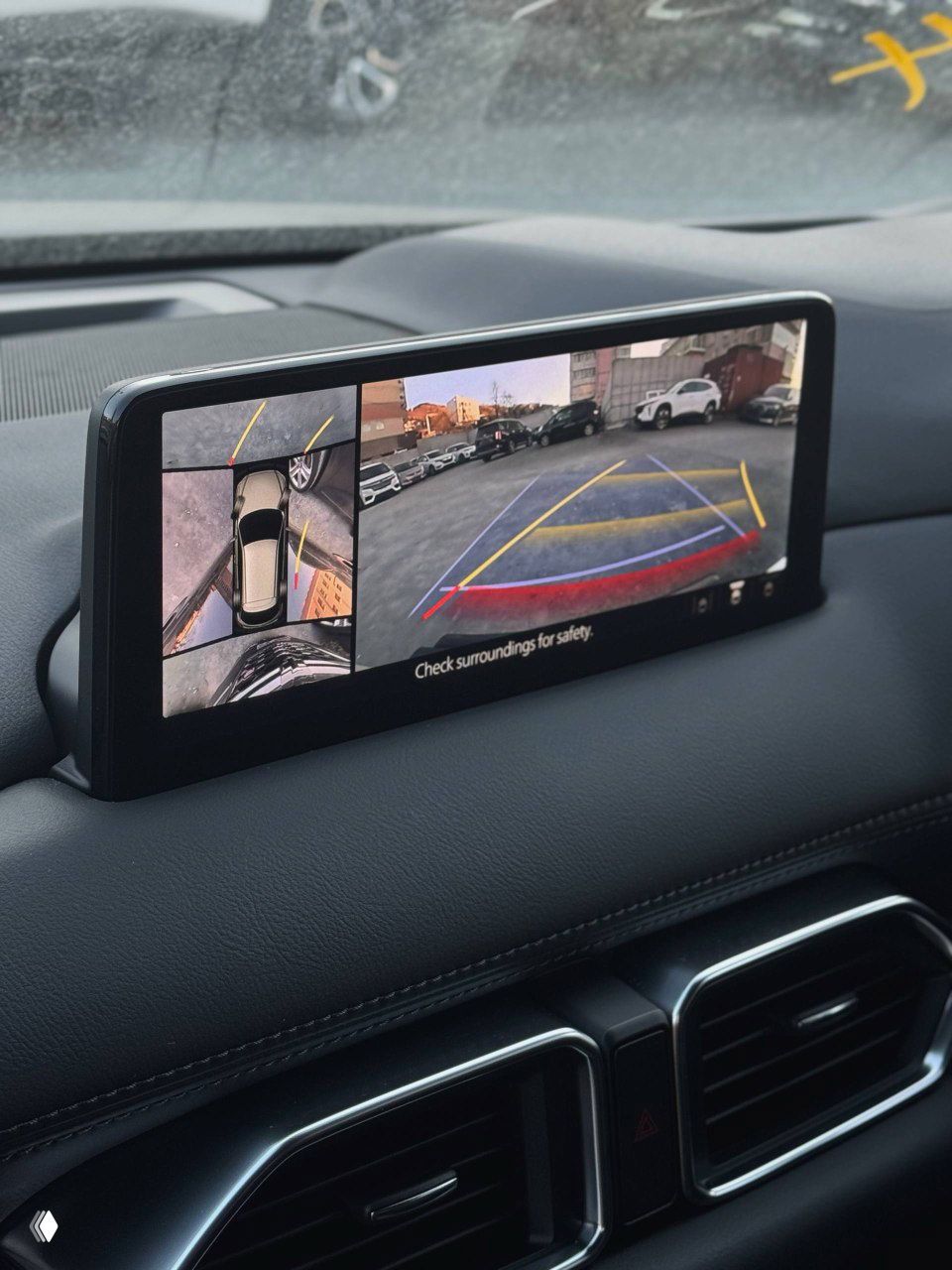 Штатный экран мультимедиа Mazda CX-5 с отображением камеры заднего вида и обзором сверху — изображение парковочной зоны и подсказки безопасности.