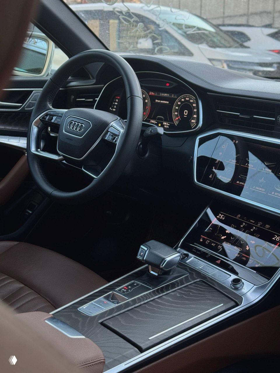 Рулевое колесо и цифровая приборная панель Audi A6, коричневый кожаный салон виден на заднем плане; фото салона перед импортом в Москву.
