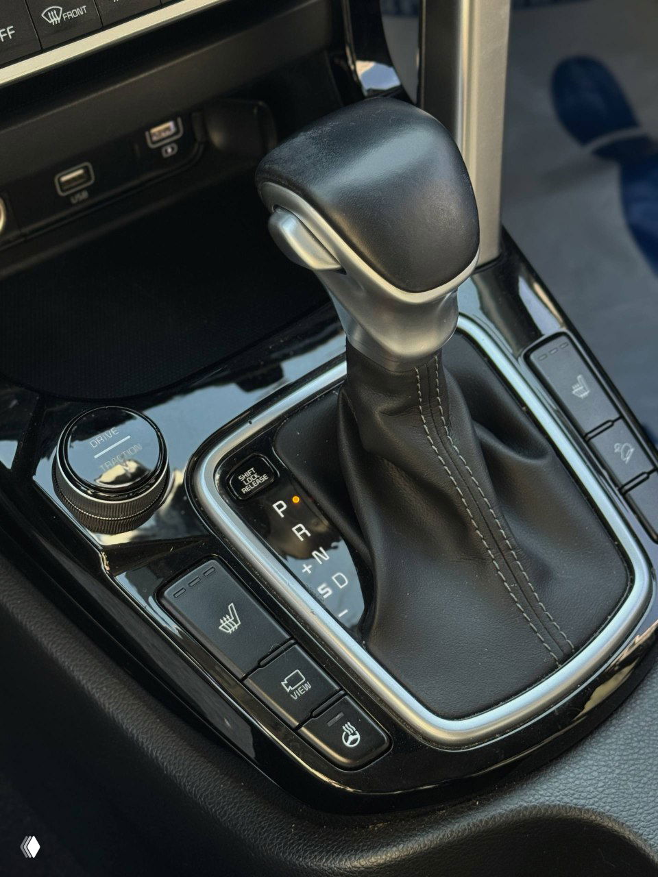 Крупный план селектора АКПП KIA Seltos и окружающих кнопок (подогрев, режимы движения), чёрная глянцевая панель вокруг рычага