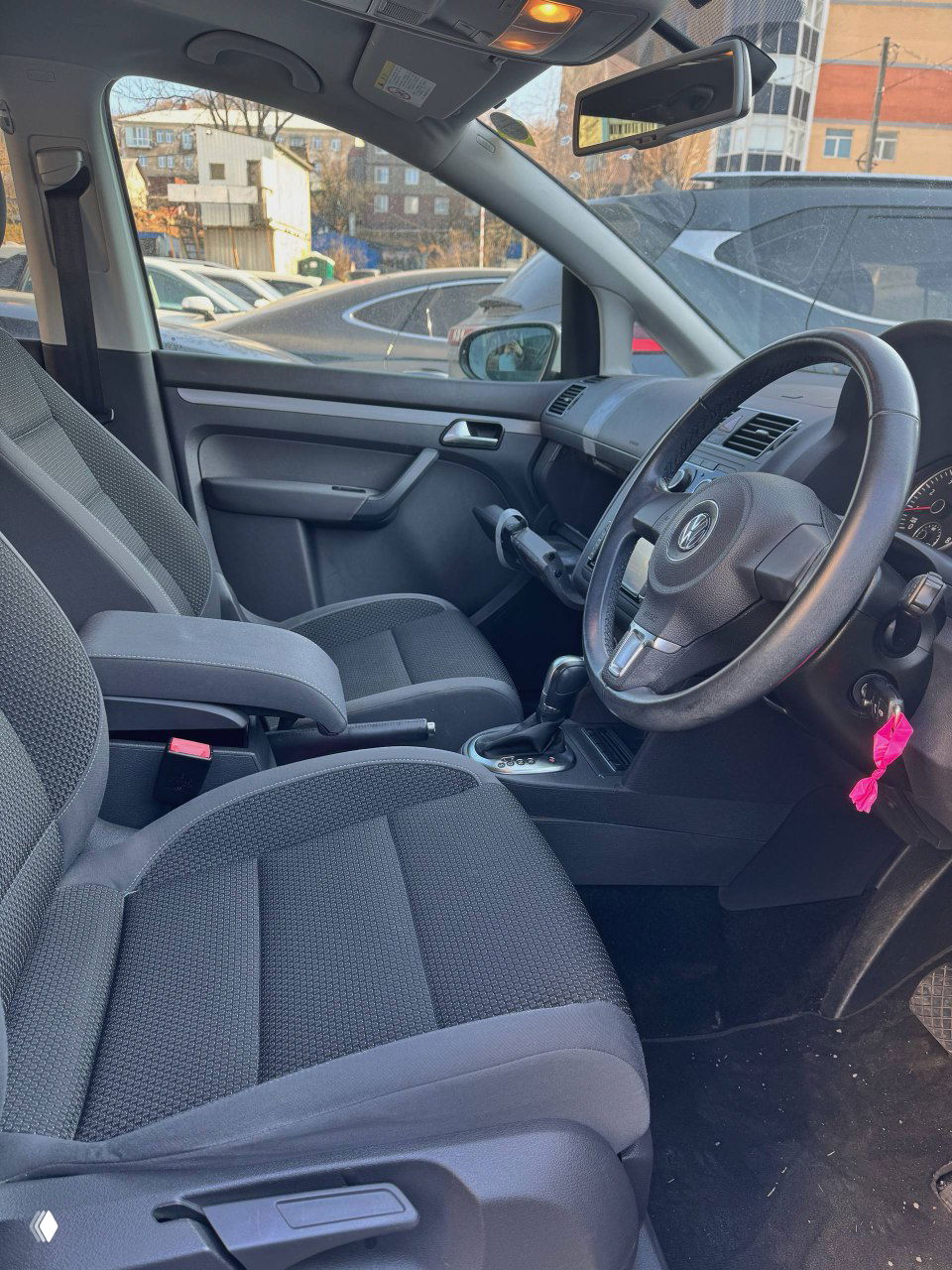 Передние сиденья Volkswagen Touran 2014 с тканевой обивкой, центральный подлокотник, рычаг ручного тормоза и общий вид водительской зоны салона.