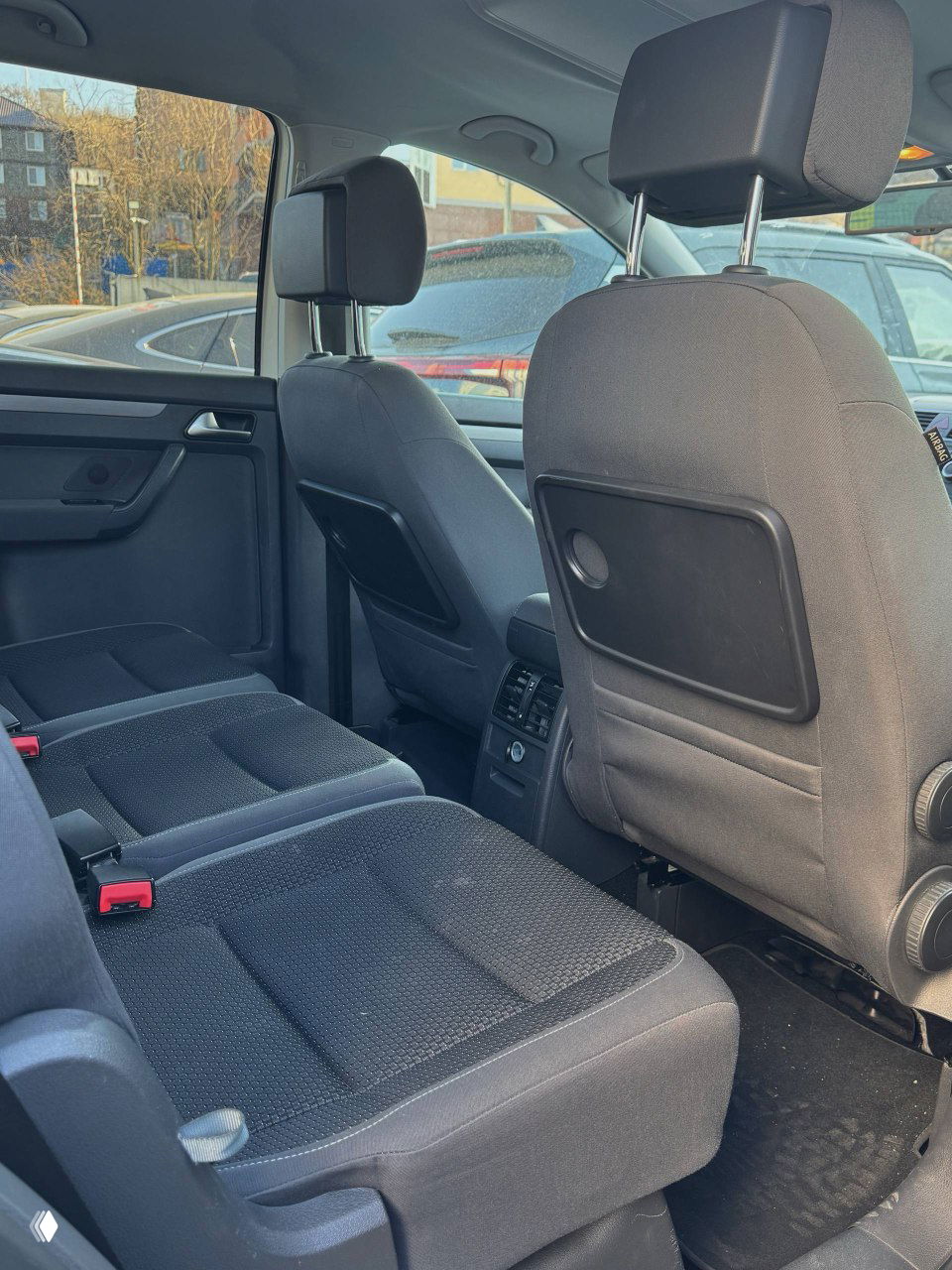 Задний ряд сидений Volkswagen Touran: три отдельных места с тканевой обивкой, столики на спинках передних кресел и пространство для пассажиров.
