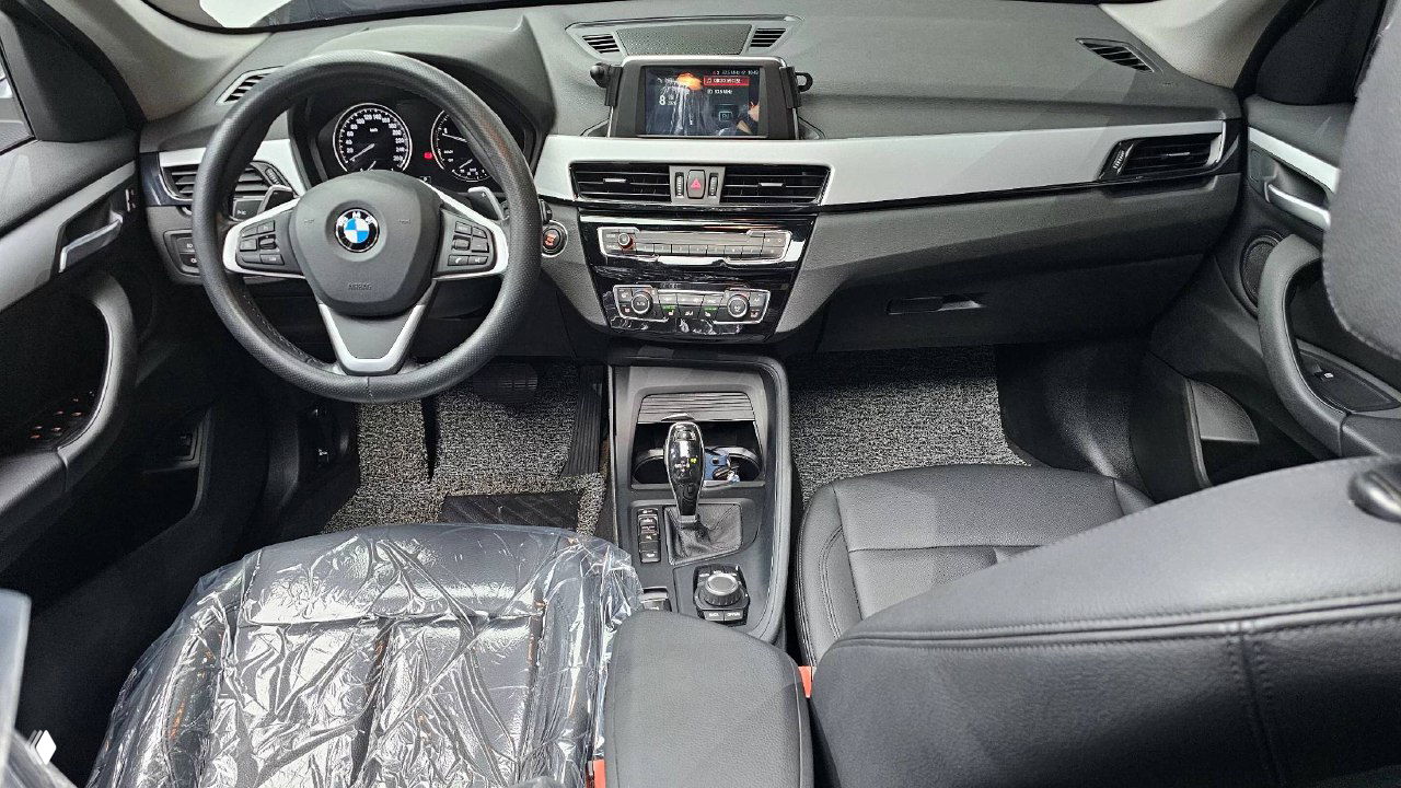 Интерьер BMW X1: вид на руль, приборную панель, центральную консоль и мультимедийный дисплей; кресла в хорошем состоянии.