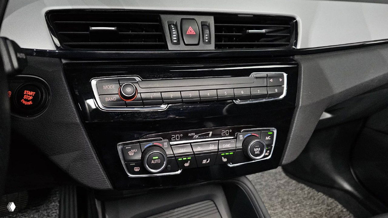 Блок климат-контроля и панель управления в BMW X1, крупный план кнопок, регулировок температуры и индикаторов в салоне.