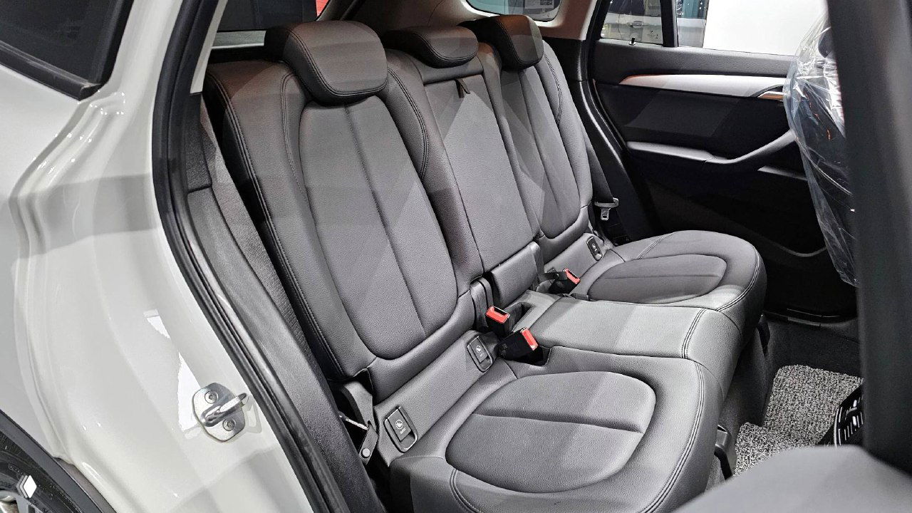 Задний ряд сидений BMW X1: три посадочных места, ремни безопасности и состояние обивки, общий вид салона с открытой дверью.