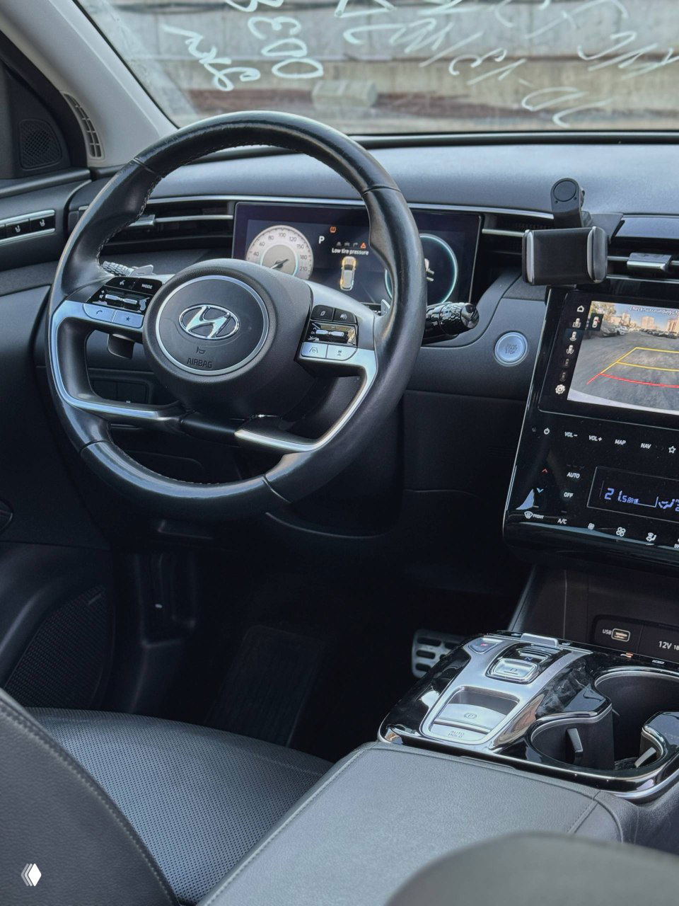Рулевое колесо и приборная панель Hyundai Tucson, вид на цифровую панель приборов и центральный дисплей, салон в чёрной отделке.