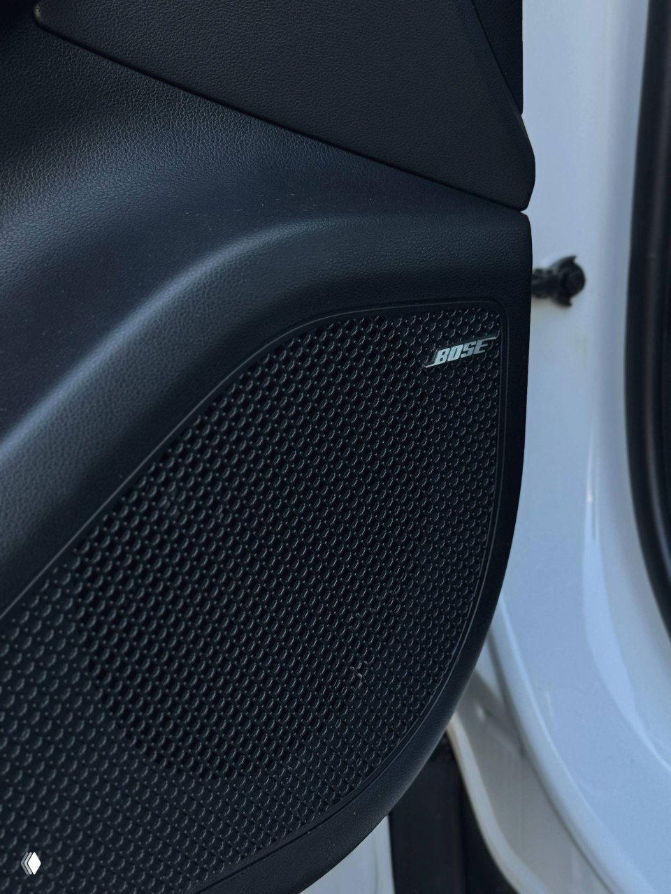 Динамик Bose на двери Hyundai Tucson, крупный план решётки акустики с логотипом BOSE на передней двери автомобиля светлого цвета.