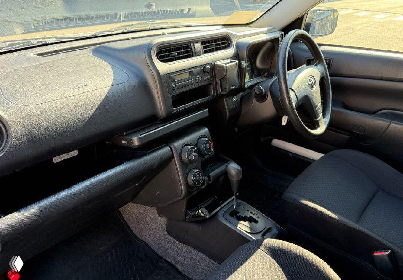 Салон Toyota Succeed: торпедо, рычаг КПП и передние сиденья, видно состояние приборной панели и отделки в дневном свете на площадке в Японии.