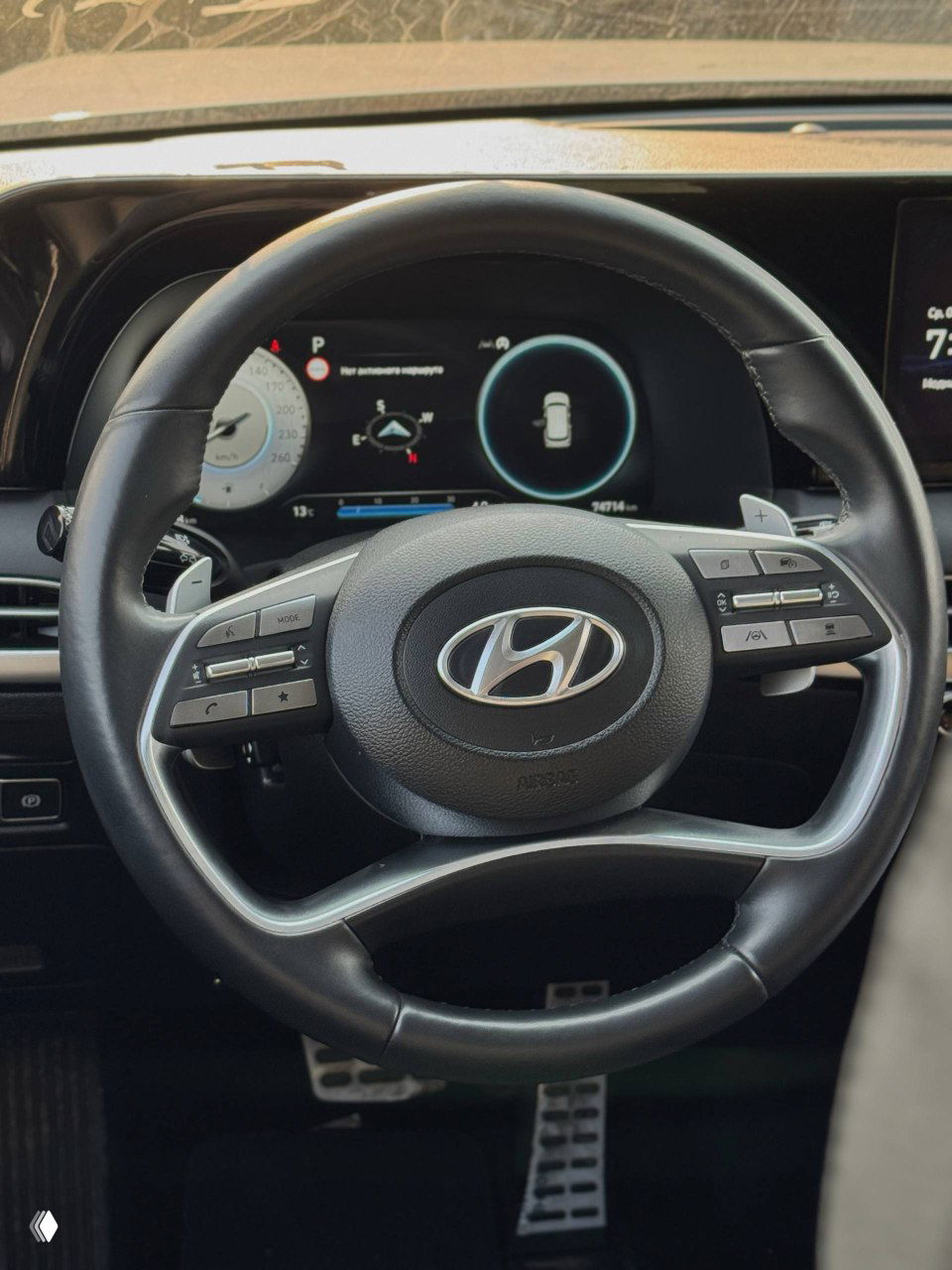 Крупный план руля и цифровой приборной панели Hyundai Palisade — вид салона, логотип Hyundai на руле и мультимедийная панель на заднем фоне.