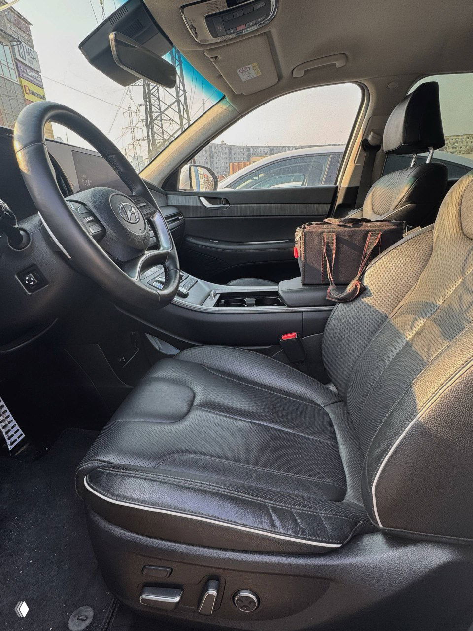 Вид на передний салон Hyundai Palisade — пассажирское и водительское места, центральная консоль и часть лобового стекла при дневном освещении.