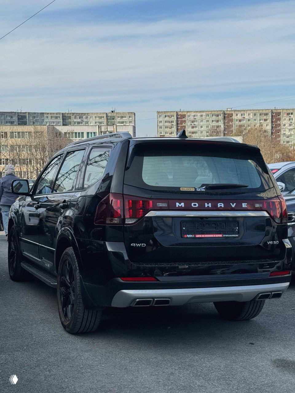 Задняя часть KIA Mohave 2020 чёрного цвета: надпись MOHAVE на багажнике, двойные выхлопные насадки и шильдик 4WD, автомобиль на парковке.