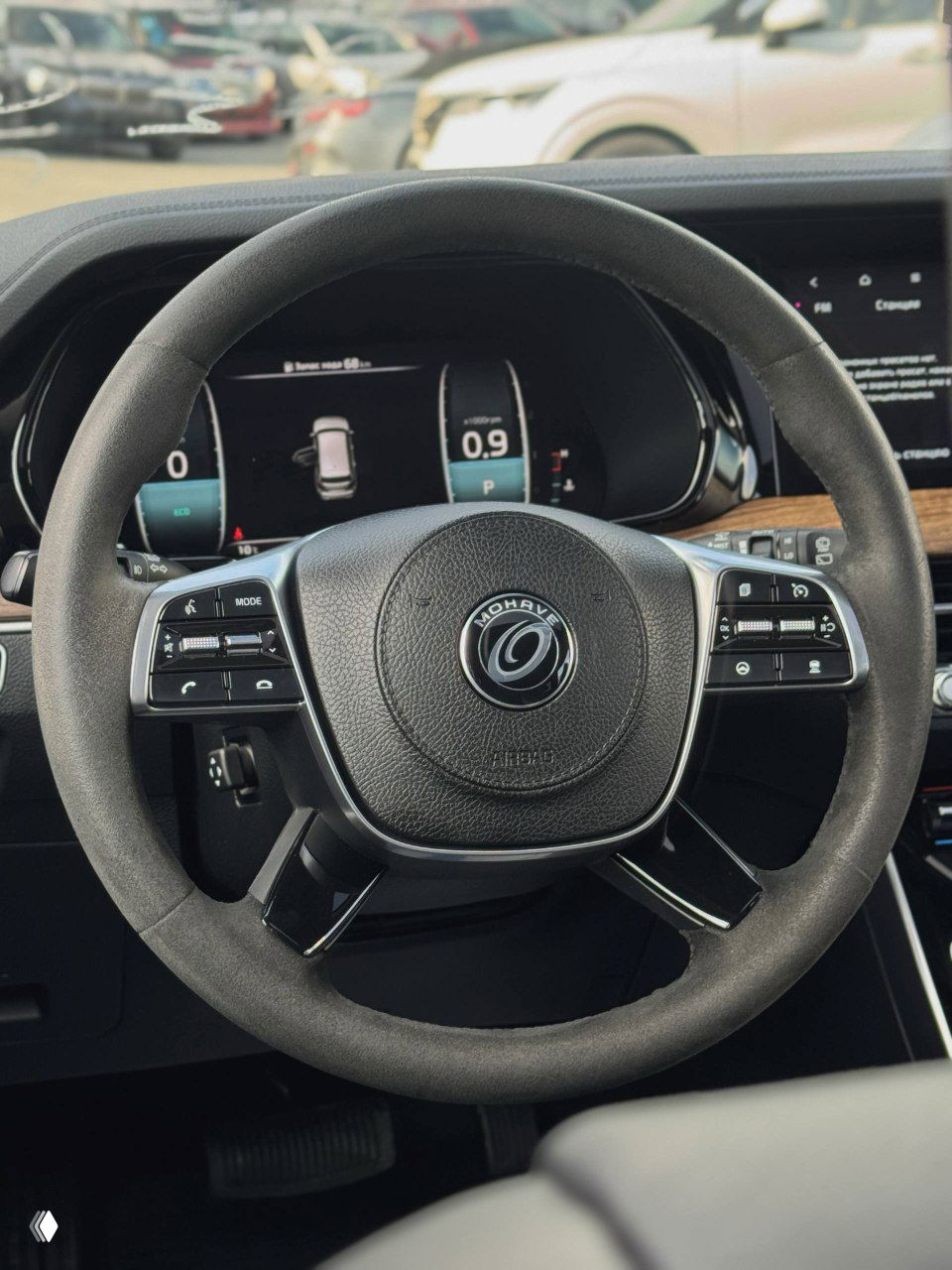 Руль KIA Mohave с мультирулевыми кнопками и логотипом Mohave в центре, цифровая приборная панель и часть передней панели автомобиля.