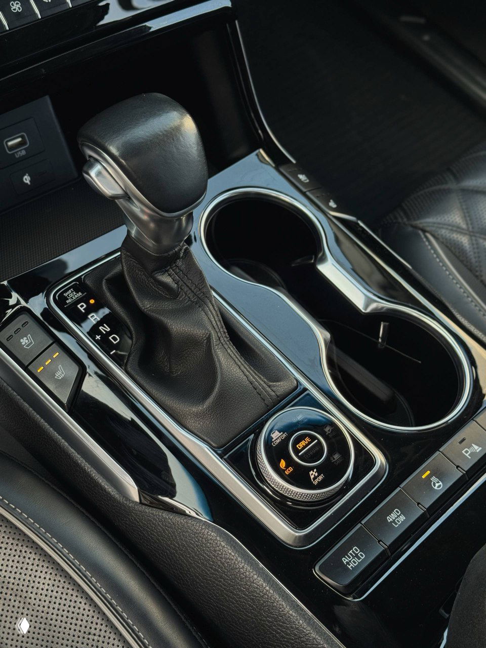 Селектор коробки передач и подстаканники в KIA Mohave: вид крупным планом на рычаг, селектор режимов движения и элементы управления около него.