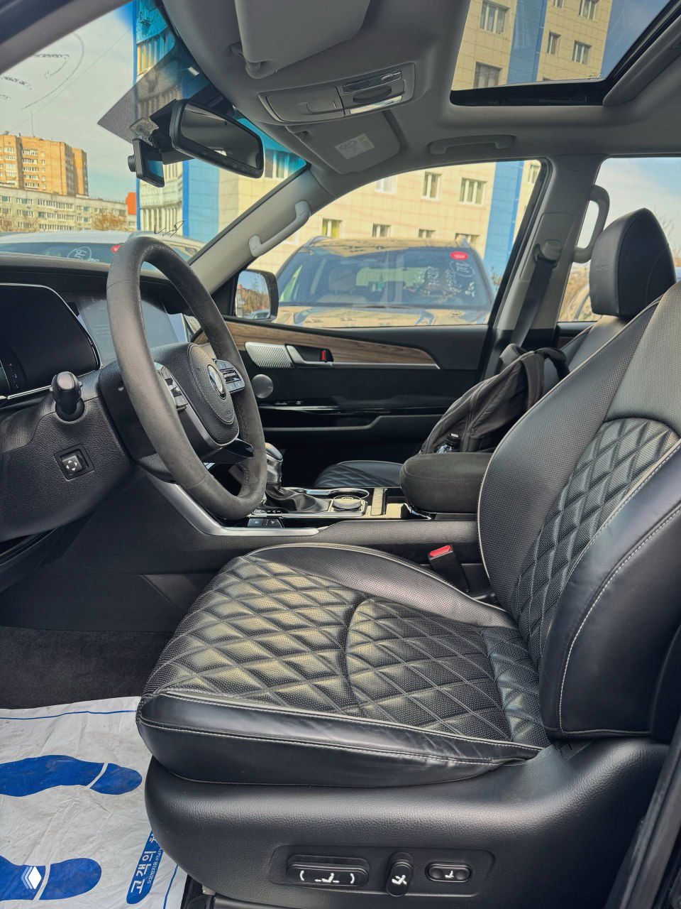 Вид на переднее пассажирское место KIA Mohave: кожа чёрного цвета, регулировки сиденья, панорамный люк и общий интерьер с водительского места.