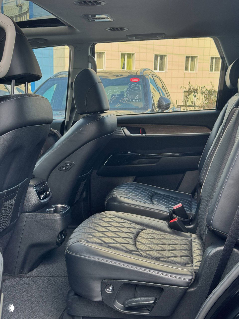 Второй ряд сидений KIA Mohave: два отдельных комфортных кресла с кожаной обивкой и простор для пассажиров, элементы отделки двери видны.