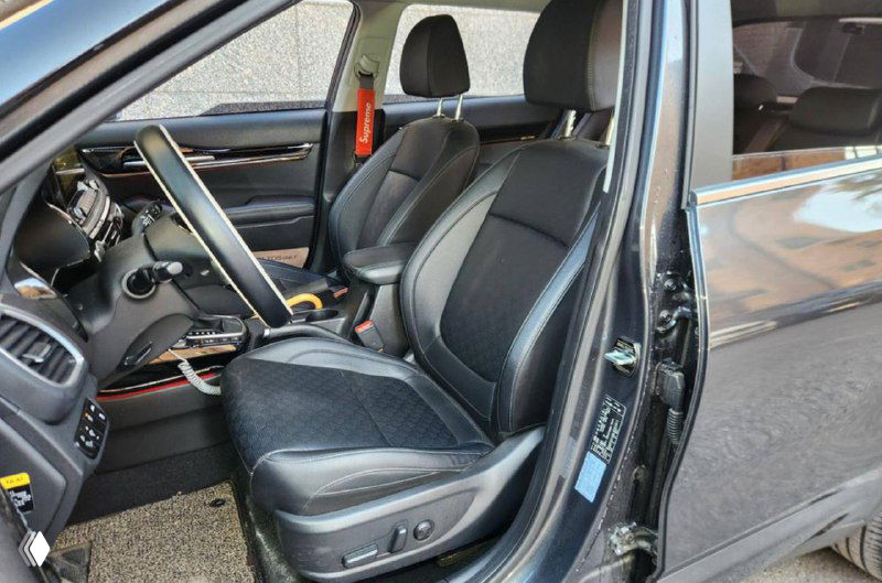 Фотография переднего сиденья и дверного проёма KIA, видны электрические регулировки и чёрная тканевая отделка сидения, фотография сделана при дневном свете.