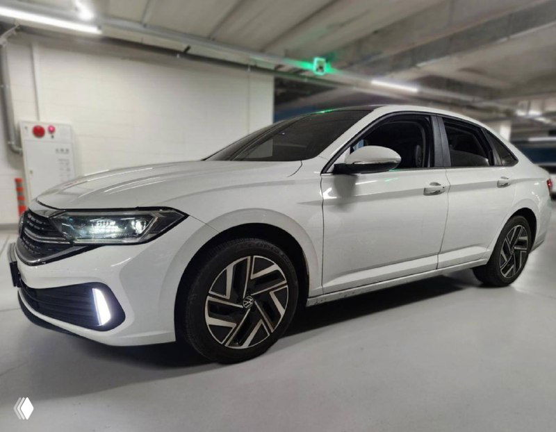 Белый Volkswagen Jetta снят в подземной парковке: боковой и фронтальный вид, чётко видны фирменные фары и дизайн передней части кузова.