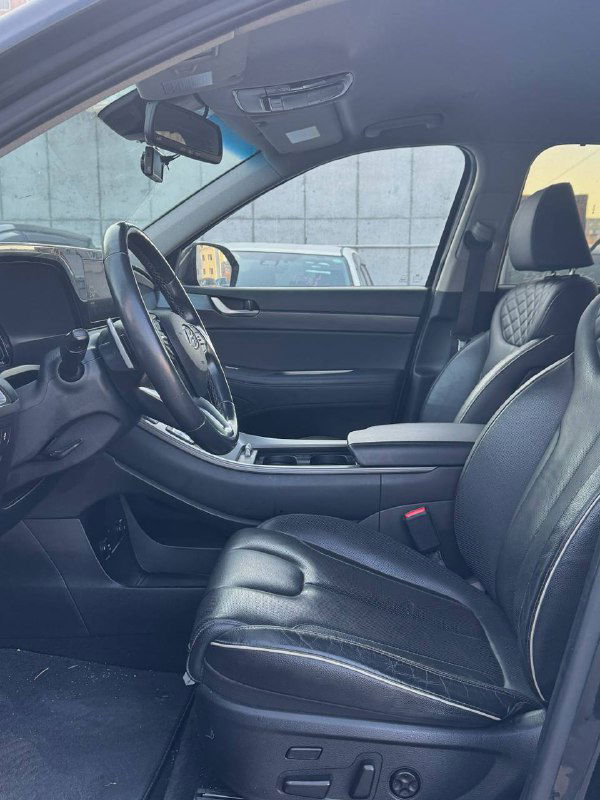 Вид на передний ряд сидений и пассажирскую зону Hyundai Palisade, кожаные сиденья, центральный подлокотник и общее состояние салона водителя и пассажира.