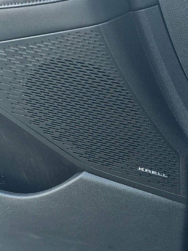 Деталь дверной обивки с динамиком марки Krell или похожего бренда, крупный план решётки акустического динамика и текстуры отделки салона Hyundai Palisade.