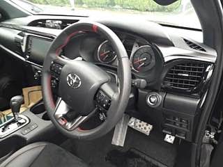 Интерьер Toyota Hilux: рулевое колесо справа, приборная панель и мультимедиа, алюминиевые педали и спортивные акценты в салоне.