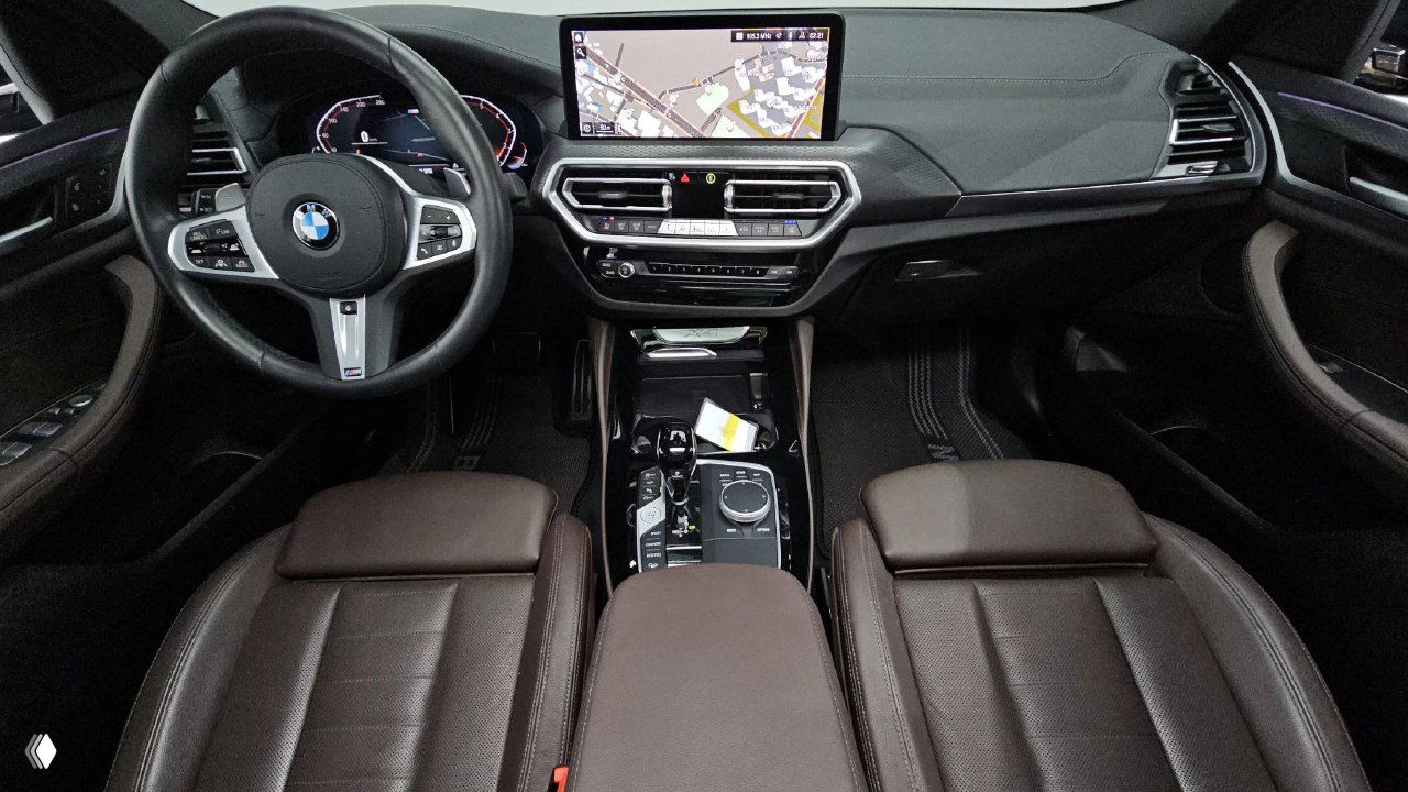 Салон BMW X4: панорамный вид на руль, центральную консоль с экраном навигации и коричневую кожаную обивку передних сидений высокого качества.