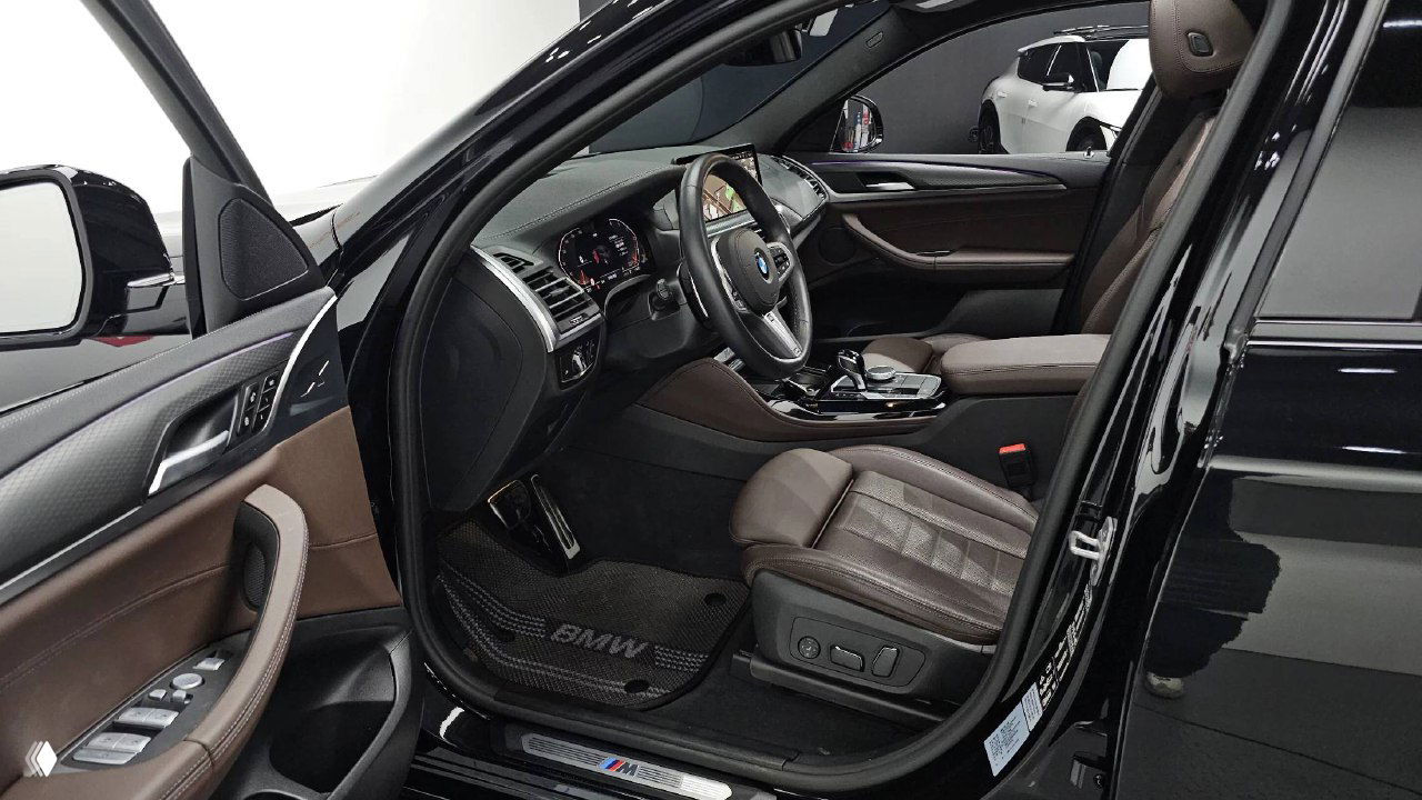 Открытая водительская дверь BMW X4 с видимым сиденьем, подножкой и элементами управления — коричневая кожа и декоративные вставки в дверной панели.
