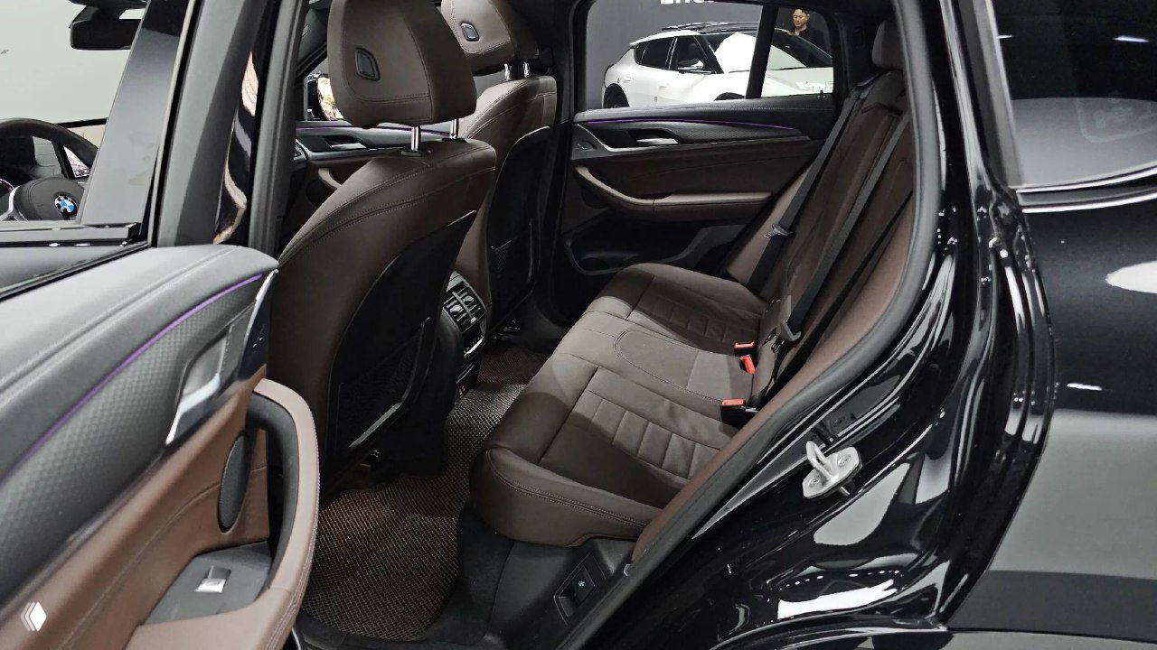 Задний ряд сидений BMW X4 с коричневой кожаной обивкой, виден комфортный подлокотник и пространство для ног, состояние обивки аккуратное.