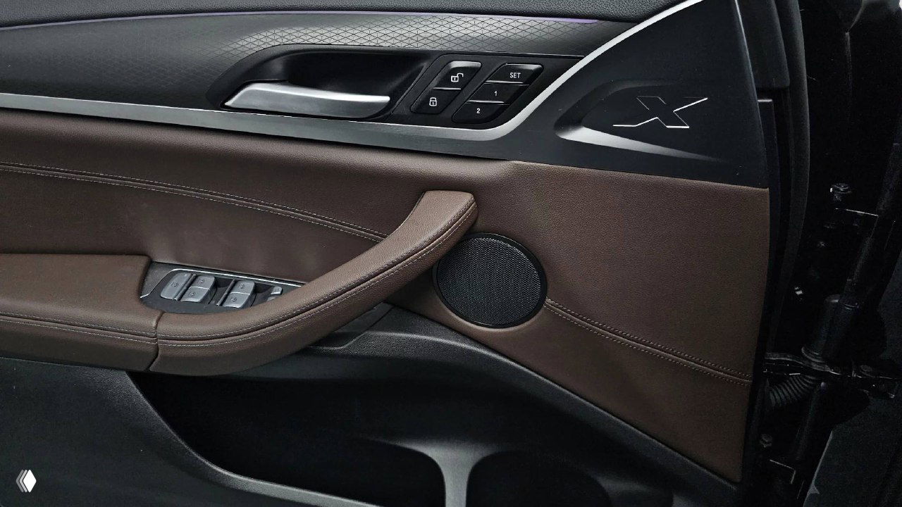 Дверная панель BMW X4 с декоративной строчкой, кнопками управления стеклоподъёмниками и декоративной эмблемой X на вставке, коричневая отделка.