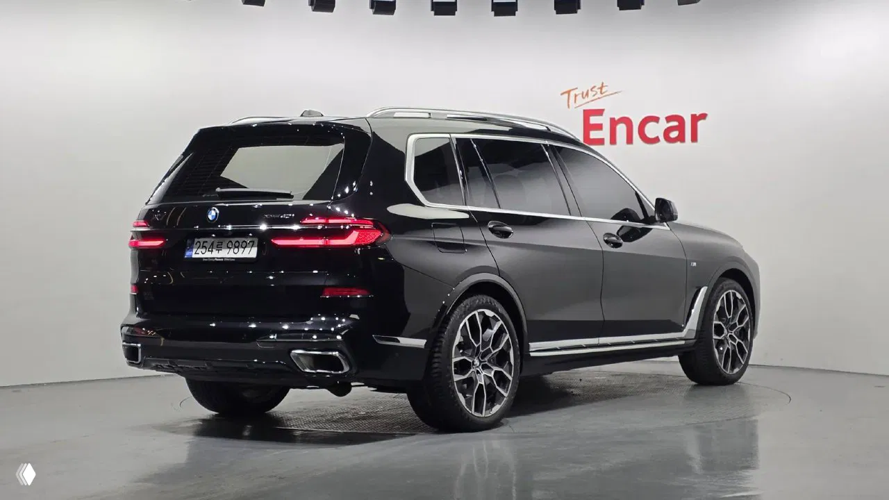 Задний трёхчетвертной ракурс BMW X7 xDrive 40i M‑Sport в чёрном цвете, видны задние фонари, патрубки выхлопа и номер Южной Кореи.