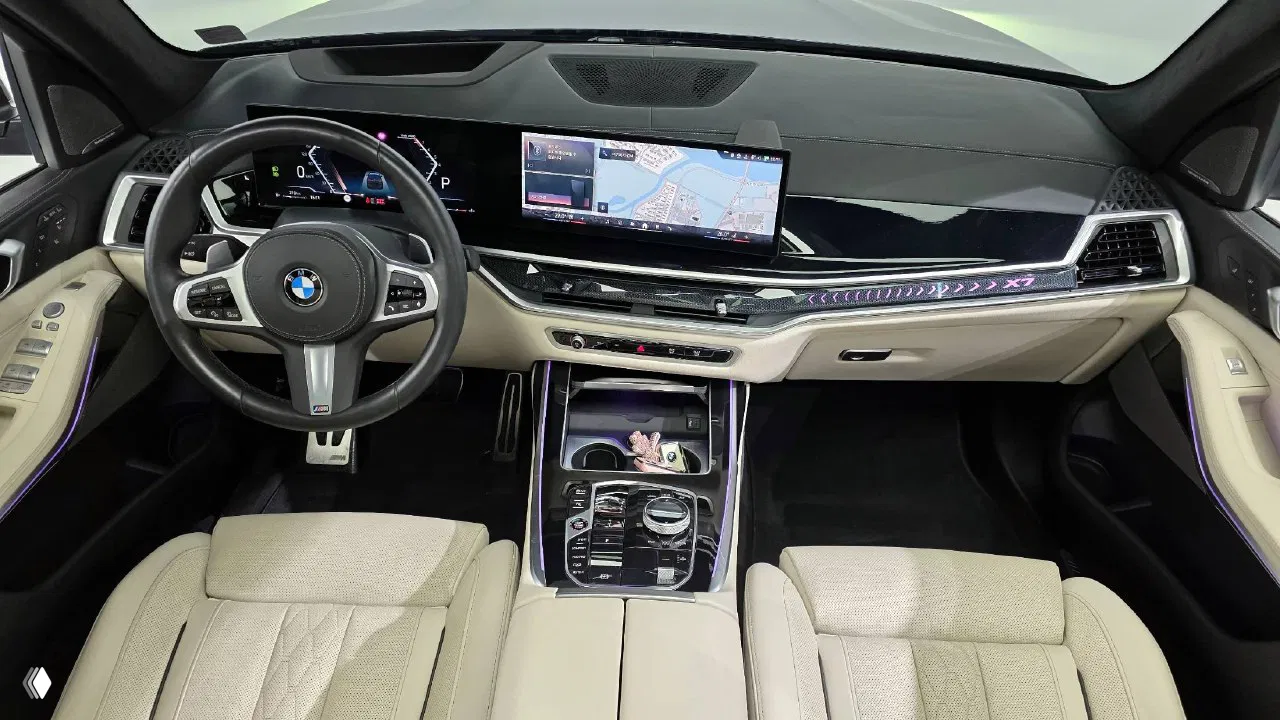 Интерьер BMW X7: передняя панель, широкий дисплей мультимедиа и навигации, центральная консоль с элементами управления и светлой кожаной обивкой.