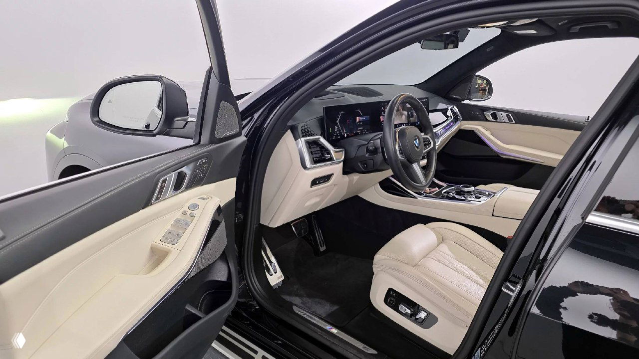 Открытая передняя дверь и водительское место BMW X7: вид на сиденье с бежевой кожей, панель управления дверью и порог с логотипом.