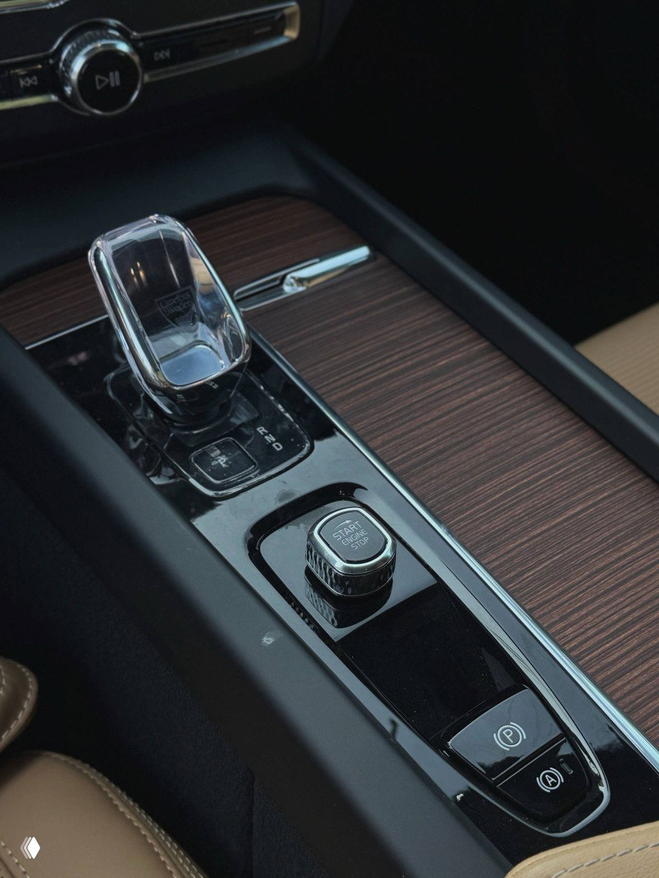 Кристаллическая ручка переключения передач и кнопка Start/Stop на центральной консоли Volvo, заметны вставки под дерево и глянцевый лак.