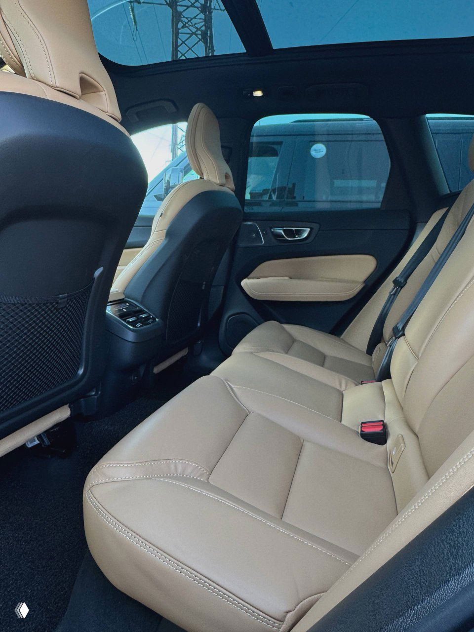 Задний ряд сидений Volvo XC60 бежевого цвета, видна просторная подножная зона, ремни безопасности и отделка дверей с динамиком.