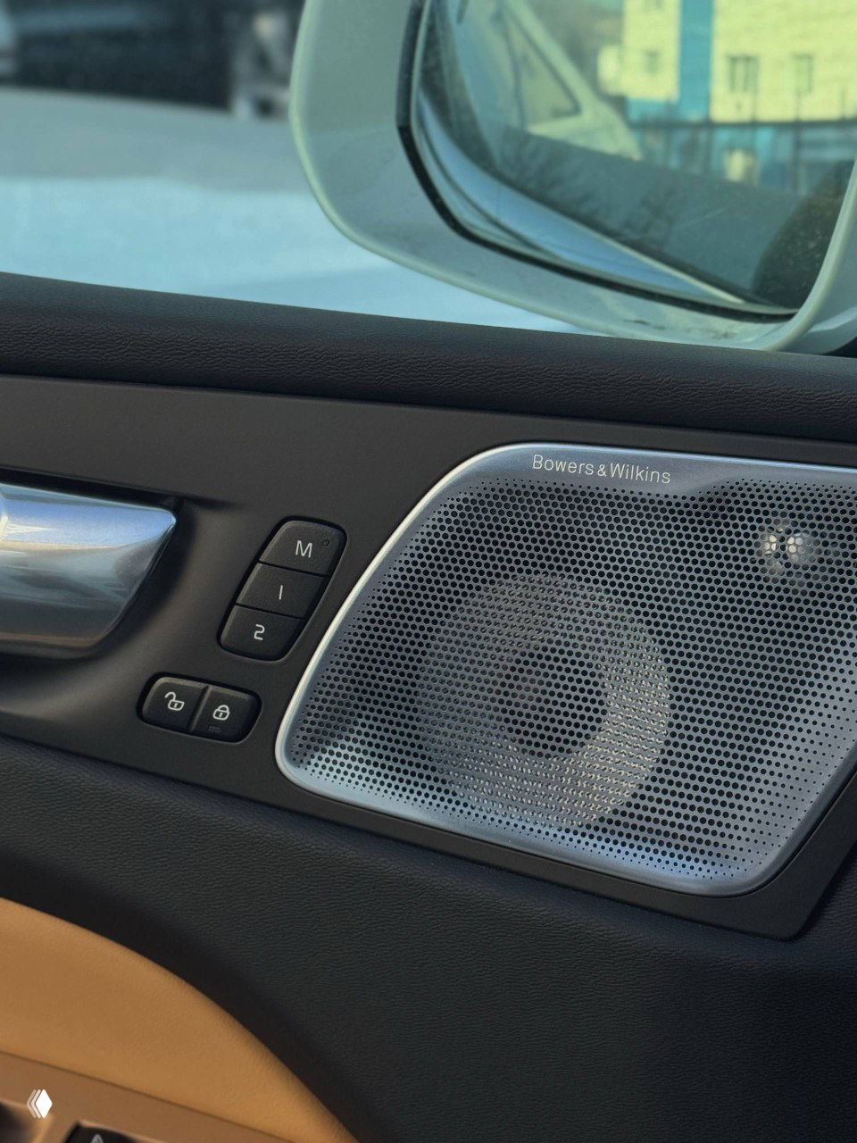 Крупный план акустической решётки Bowers & Wilkins в двери Volvo, логотип бренда, материалы отделки и кнопки памяти сиденья.