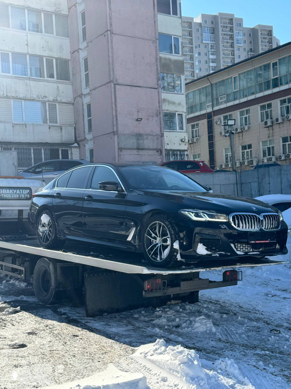 BMW 520i уже на платформе эвакуатора: чёрный седан установлен на причале эвакуатора, снег на бортах и колёсах виден отчётливо.